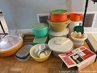 Assorted plastic food storage containers in various colors and sizes, including a food chopper and a boxed Sunbeam hand mixer.