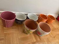 Set of 7 small ceramic plant pots in various colors and patterns arranged on a floor.