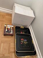 Photo showing two black nesting trays with floral designs and yellow handles stacked inside each other next to the punch bowl box and wine bottle sealer box.