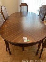Full view of oval-shaped solid wood dining table with four chairs, showing tabletop and legs.