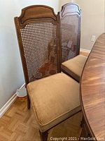 Front and side view of matching wooden dining chairs with cane back and padded beige seat, showing carved wood legs and wear.