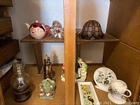 Overview of shelf with multiple vintage items including oil lamps, figurines, and a stained glass lamp shade
