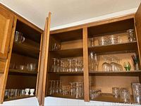 Glass and crystal glasses and bowls stored inside kitchen cabinets, showing multiple rows of stemmed liquor glasses and bowls.