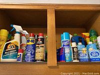 Photo showing assorted cleaning sprays including Armor All Multi-Purpose spray, WD-40, 3-IN-ONE, Lysol, and others in a wooden cabinet.