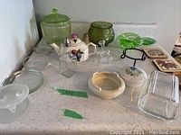 Overview of lot showing multiple glassware and ceramic items including teapot, butter dishes, bowls, and vases, arranged on countertop