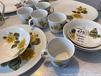 Photo showing six teacups, three bowls, and plates with yellow and green floral patterns, some with chips and wear.