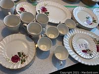 Set of multiple plates, cups, and saucers featuring a rose pattern with embossed edges and some wear visible.