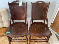 Front view of two matching antique wooden chairs showing nailhead decorative pattern and carved wood detail at top.
