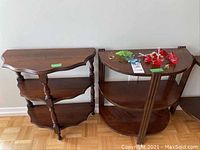 Photo showing two wooden half moon tables side by side, each with three shelves. Tables have a dark wood finish with visible wear and scratches.