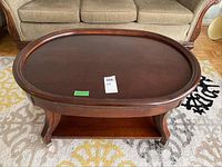 Front angle of oval wooden coffee table showing oval top and curved legs with lower shelf.