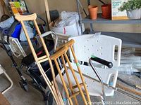 Photo of black bath chair, Nexus walker, wooden crutches, and portable toilet seat with arm supports