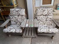 Full front view of two wooden Adirondack chairs with floral cushions connected by a wooden slatted table.