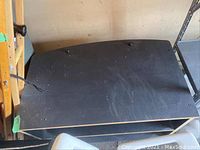 Black TV stand with two open shelves, surface shows scratches and dust