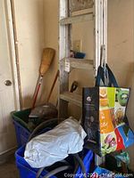 Photo of 5-step aluminum ladder leaning against wall with broom, shovel, green bin with tools, and reusable shopping tote bag.