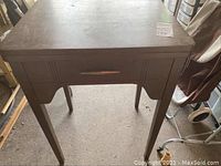 Wooden sewing machine table with visible drawer and legs, photographed in ambient lighting indoors.