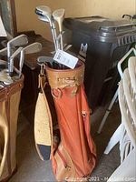 Photo showing golf clubs inside a brown and tan golf bag with shoulder strap and multiple clubs with metal heads.