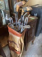 Full view of vintage golf clubs standing in a beige and brown golf bag beside furniture indoors.