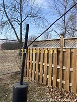 Black metal bird feeder mounted on a 73-inch tall black pole with a weighted round base outdoors by a wooden fence.