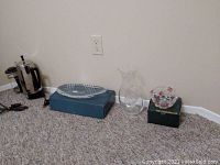 Six glass and kitchen-related items arranged against a wall on carpet: French press, Villeroy & Boch dish in a box, glass decanter, Waltherglas bowl in a box