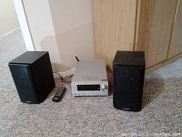 Front view of Sharp stereo main unit with two speakers and remote on carpeted floor.