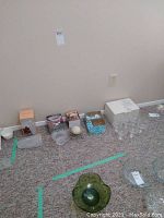 Wide view of all crystal and glass items lined up on carpeted floor against beige wall, including a green glass bowl and several clear glass pieces.