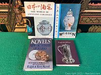 Five antique collector guide books displayed on a table with an oriental backdrop, titles visible: Japanese Ceramics, Meissen, Kovels marks, and English Silver.