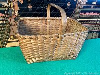 Full side view of old rectangular Native American oak split wood basket with handle, showing woven construction and color.