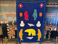 Full view of vintage Inuit wall hanging tapestry with multiple colorful appliquéd figures and animals on dark blue fabric.