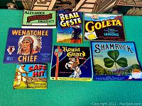 Top view of seven vintage lithographed crate labels laid flat showing bright graphics and colors.