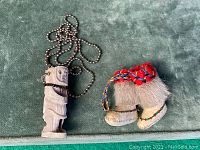 Photo showing both the carved pendant necklace and miniature mukluks on a green fabric background.
