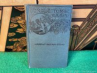 Front cover of the blue hardcover book Uncle Tom's Cabin showing embossed illustration and title.