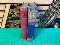 Side view of the two books standing upright showing spine titles and cover colors (red and blue).