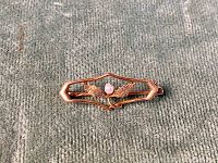 Top view of antique 10k gold brooch with central pearl and leaf design on grey textured fabric.