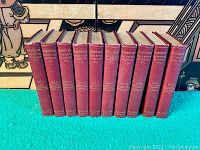 Front view of ten red hardcover Shakespeare volumes arranged side by side, showing gilded spines with volume numbers and titles