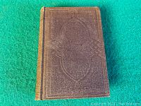 Front cover of the book showing dark brown textured cover with embossed decorative design.