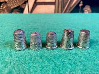 Front view of five thimbles aligned in a row on green felt
