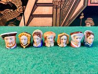 Full view of the 7 figural thimbles arranged in a row on green surface.