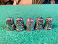 Front view of five silver thimbles upright showing decorative patterns