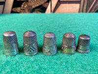 Front view of five sterling silver thimbles showing tops and decorative bands
