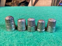 Side view of five silver thimbles lined up on green felt