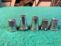 Front view of five thimbles on green felt; shows overall shapes and decorative details