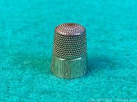 Front view on teal background showing beaded dome top and engraved lower band