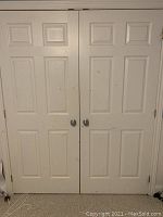 Photo of two white paneled closet doors side by side with door knobs and trim, showing surface scratches and marks.
