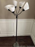 Full view of the 5-arm floor lamp with white frosted glass cone-shaped lampshades on a black metal stand and round metallic base