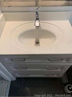 Top view showing white solid surface countertop with integrated oval sink and single-handle chrome faucet, three drawers below.