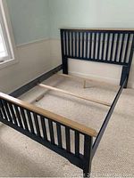 Photo of black wooden queen bed frame showing headboard, footboard, side rails, and wood support slats on carpeted floor.