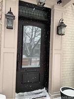 Exterior view of black exterior door in doorway with snow falling