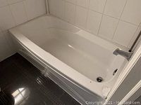 Photo of a white bathtub with attached chrome faucet and surrounding tiled wall and floor