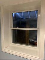 Photo showing one vinyl window mounted in a wall, white frame and trim, double-hung sash style, with clear glass.