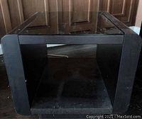 Front view of one of the smaller square dark wood side tables with glass top showing the design and scratches on the wood surface.